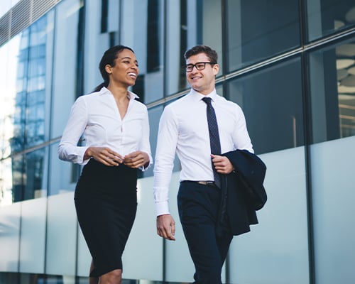 Contemporary elegant diverse woman and man smiling happily while talking and walking on street on background of modern glass building